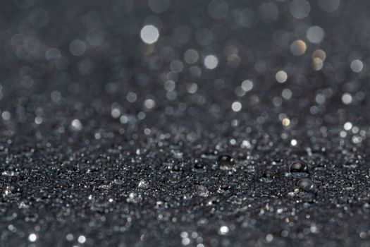 dark grey water resistant hydrophobic flat cloth with rain drops, close-up background with selective focus and bokeh blur