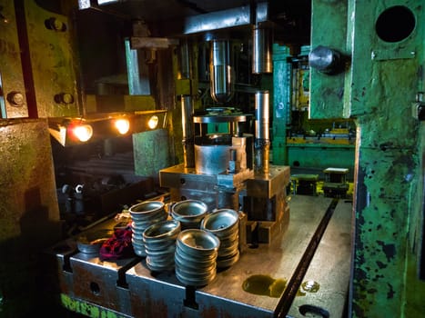 dirty used low tech stamping press producing round aliminium parts in dark environment.