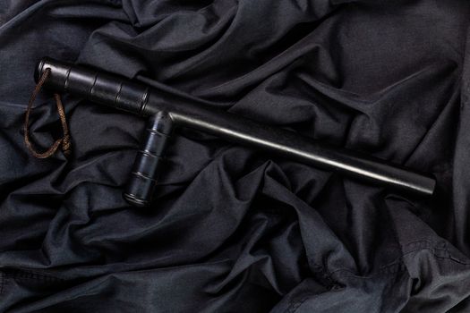 black rubber police baton on black shirt wrinkled cloth low-key flat lay.