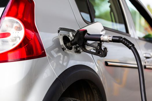 gray metallic car refueling on gas station - closeup with selective focus and blurry man on background.