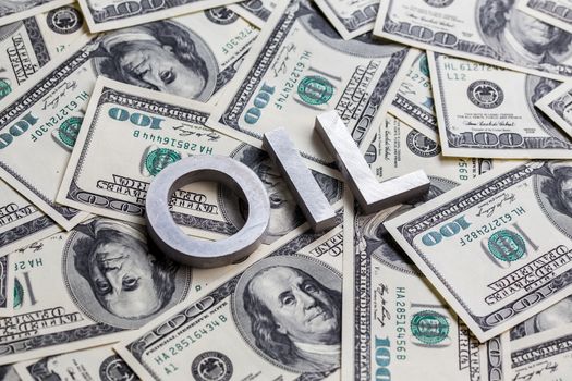 The word OIL laid with aluminium letters on the US dollar banknotes background - with selective focus and diagonal composition.