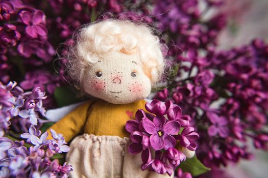 Little golden-haired angel in the blue, pink, purple, violet lilac flowers. Handmade toy in violet lilac colors.