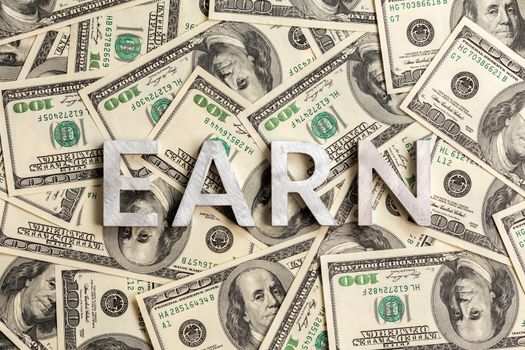 The word earn laid with aluminium letters on the US dollar banknotes background - with selective focus and diagonal composition.