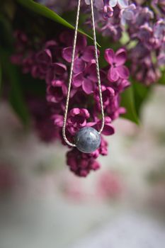 Original silver jewelry necklace made of natural stone with purple violet lilac flowers on white ostrich feather. Gift concept. Silver accessories. Mock up space for text.