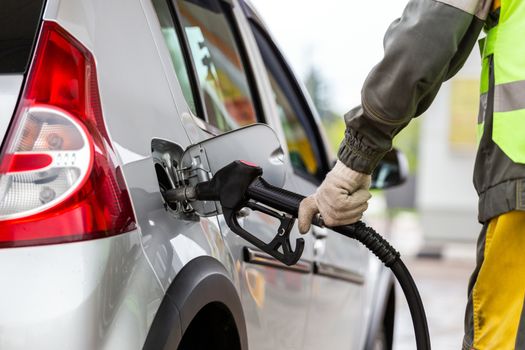 hand in white cotton fabric glove refueling gray metallic car on gas station - close-up with selective focus and blur