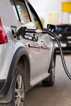 Gray metallic car refueling on gas station - closeup with selective focus and blurry man on background. Vertical orientation.