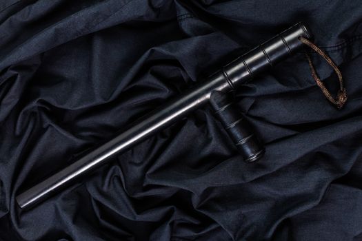 black rubber police baton on black shirt wrinkled cloth low-key flat lay.