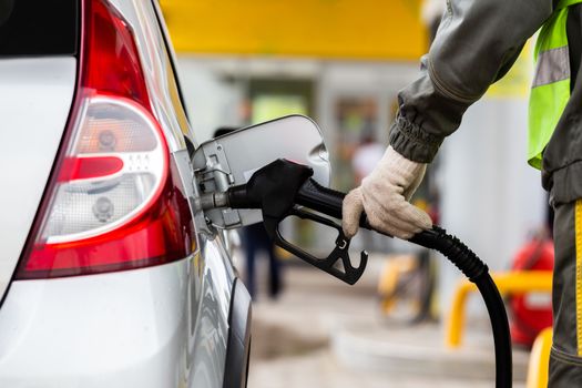 hand in white cotton fabric glove refueling gray metallic car on gas station - closeup with selective focus and blur