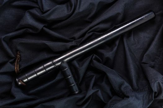 black rubber police baton on black shirt wrinkled cloth low-key flat lay.