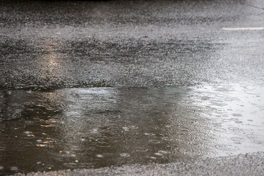puddle on asphalt road at daylight rain in city with selective focus and boke blur.