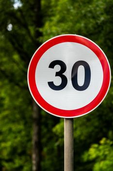 Road sign speed limit 30 kilometers per hour on green forest background with selective focus. End of youth symbol too. Vertical orientation.