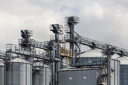 metal grain silos with elevator loading clonstructions at cloudy daylight.