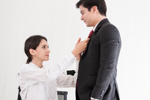 Wife tying red necktie to her husband in the office with smiling and happy.