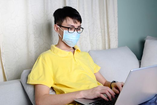 An asian man is working from home during pandemic coronavirus  Covid-19. Ccoronavirus covid 19 infected patient in quarantine room using computer.



