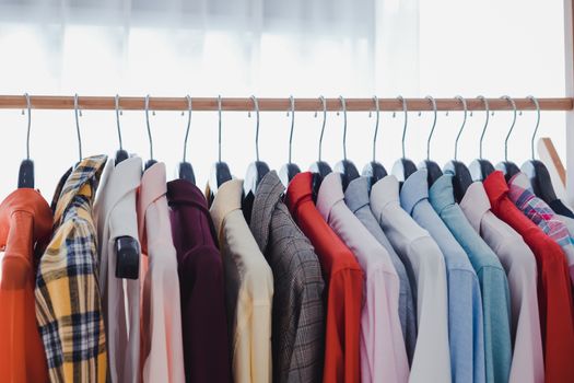 Variety and modern fashion clothes, orderly hanging on the clothesline. Clothes hang on shelf in a designer clothes store. Row of clothes hanging on rack. Fashion trend concept.