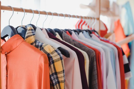Variety and modern fashion clothes, orderly hanging on the clothesline. Clothes hang on shelf in a designer clothes store. Row of clothes hanging on rack. Fashion trend concept.