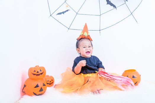 Funny happy little cute baby girl in Halloween costume with pumpkin Jack with Cobweb and black balloon in-home Halloween party on white wall background, Happy Halloween day concept