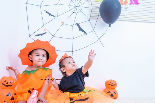 Funny happy little cute brethren baby girl and kid boy in Halloween costume with orange pumpkin Jack with Cobweb and black balloon in the home on white wall background, Happy Halloween day concept