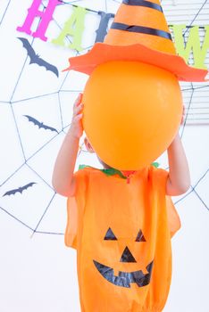 Funny happy kid boy in Halloween costume with Jack and have orange balloon on hand with Cobweb on background