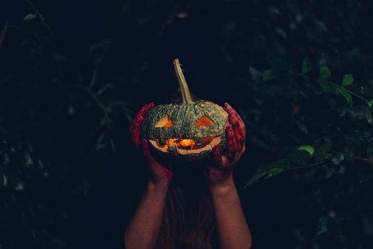 Portrait of woman devil ghost demon costume horror and scary she holding pumpkin conceal the face on hand in the forest, Happy Halloween day concept