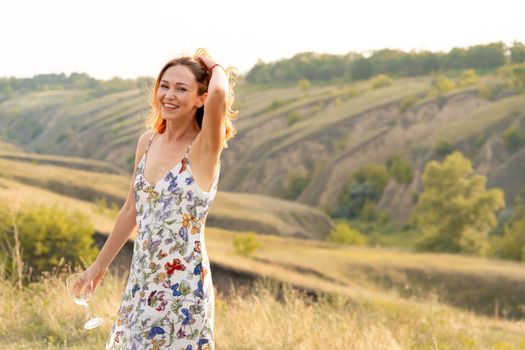 Beautiful red-haired girl is having fun and dancing in a field at sunset.