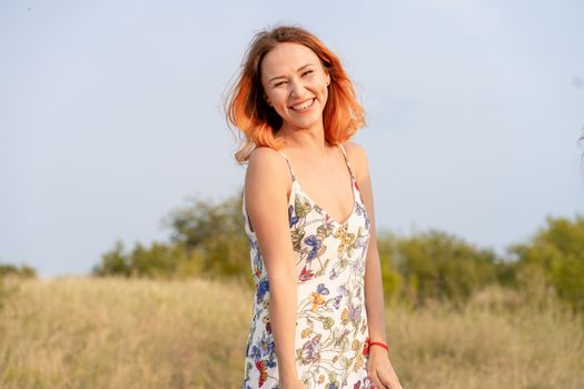 Beautiful red-haired girl is having fun and dancing in a field at sunset.