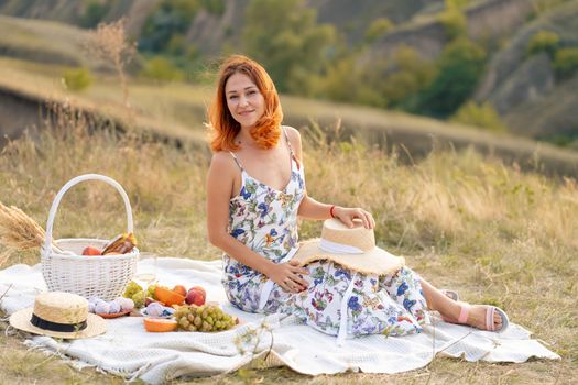 Beautiful red-haired girl enjoys the sunset on the nature. Picnic in the field