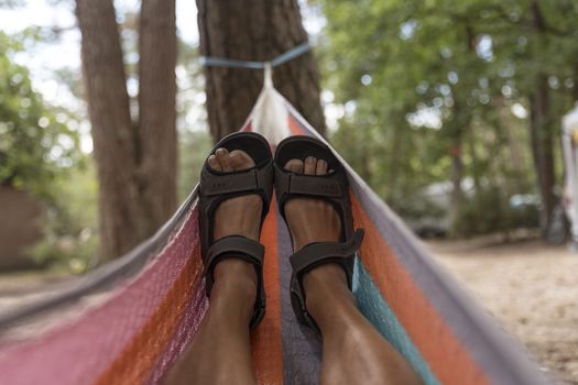 man with brown bare legs and sandals in a hammock at the campsite