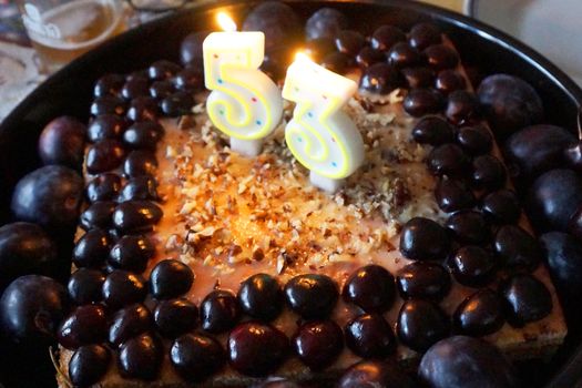 number 53 from candles on a fruit cake with cherries and plums