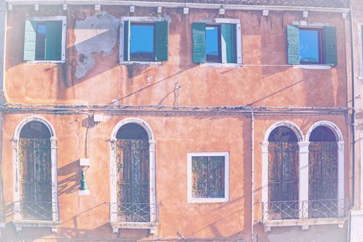 Italian culture on Venetian facades in faded color effect. Venice is rich and poor, well-groomed and abandoned, reflected in its windows.