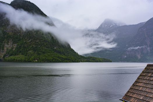  Rain and clouds on the Hallstattersee in Austria. Morning mist over the Austrian landscape with lake, forests, fields, pastures, meadows and tile roofs. 