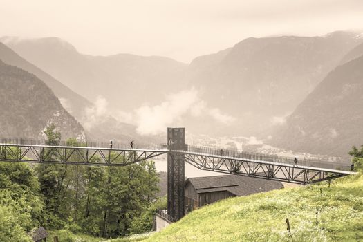 Morning mist, rain and clouds over the Austrian landscape with forests, mountains, pastures, meadows and villages.  View of the lake Hallstattersee in Austria through the pedestrian bridge. Vintage style