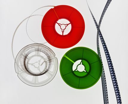 Three  film reels -white , red and green on a white background , super 8mm film strips next to the reels