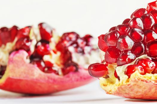 Two pomegranate sections on a white background , bright red seeds in focus ,studio shot , front view 