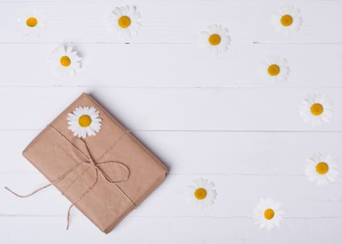 Gift box and daisy on a white wooden background