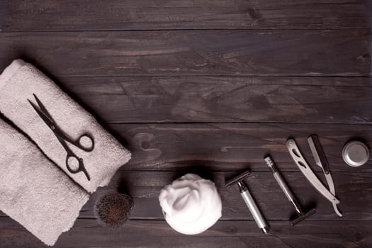 Razors, brush, balsam, perfume, towels and scissors on a wood background.