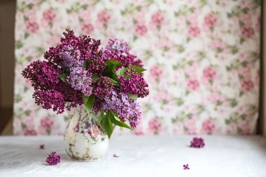 Bouquet of violet lilac in a vintage shabby vase. Still life with blooming branches of lilac in vases. Free style photo.