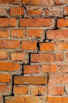 Deep cracked orange brick wall closeup texture and background. Vertical shot.