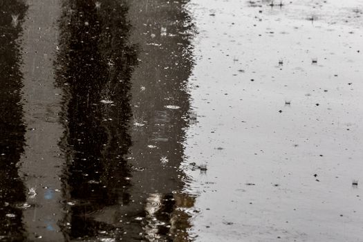 Raindrops on shiny wet flat asphalt background with selective focus and blur. Low position sharp angle telephoto shot.