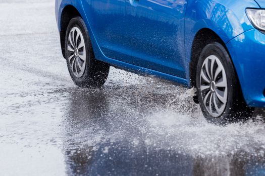 Blue car crossing puddle with water splash at daylight closeup with selective focus and blur.