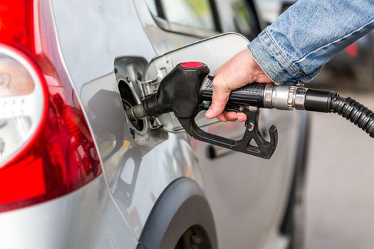 hand in jeans jacket refueling gray metallic car on gas station - closeup with selective focus and blur