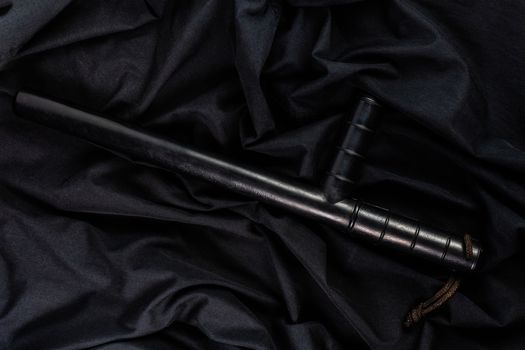 black rubber police baton on black shirt wrinkled cloth low-key flat lay.