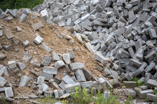 Pile of dismounted gray modern urban pavement bricks with selective focus. Result of russian government corruption in city infrastructure renovation. Piles hidden outside of city - in suburbs wasteland.