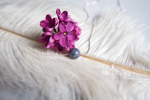 Original silver jewelry necklace made of natural stone with purple violet lilac flowers on white ostrich feather. Gift concept. Silver accessories. Mock up space for text.