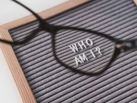 Top view on letterboard with words WHO AM I through eyeglasses. Flat lay concept of psychological self-regulation or gender identity. Social psychological issue. Closer look on psychological problems.