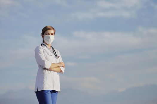Female doctor, a nurse wearing a protective face mask against blue sky with clouds. Safety measures against the coronavirus. Prevention Covid-19 healthcare concept. Stethoscope. Woman, girl.