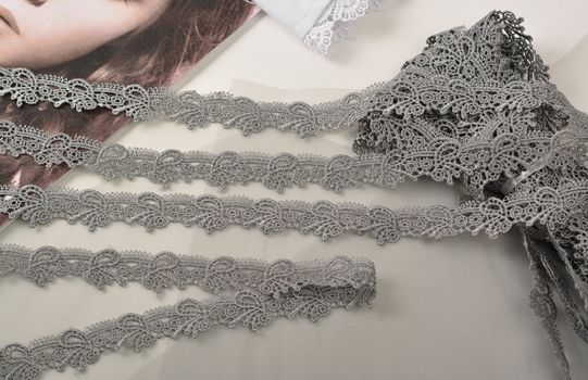 Tapes of gray gentle guipure, beauty lace fabric on light background. Elastic material. Using for Atelier and needlework store. Space for text