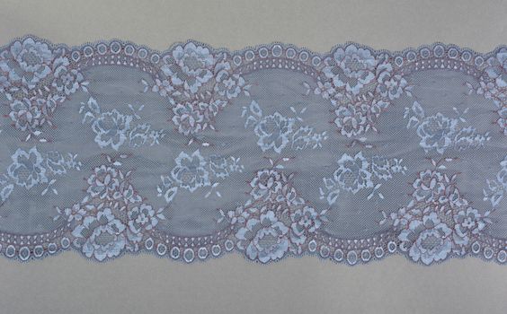 blue color straight strip of lace fabric on gray background. Elastic silk nylon braid border. use clothes linen decoration. repeating pattern and interweaving threads. texture for websites