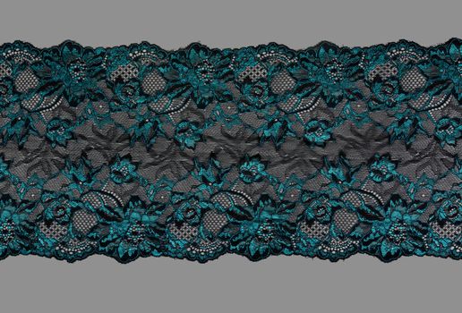 emerald black color straight strip of lace fabric on gray background. Elastic silk nylon braid border. use clothes linen decoration. repeating pattern and interweaving threads. texture for websites