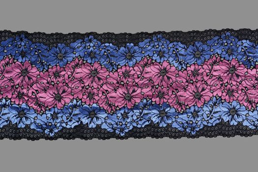blue pink black color straight strip of lace fabric on gray background. Elastic silk nylon braid border. use clothes linen decoration. repeating pattern and interweaving threads. texture for websites